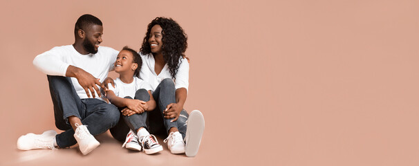 Adoption concept. Happy afro parents bonding and embracing with their adopted daughter, sitting on floor over yellow background in studio