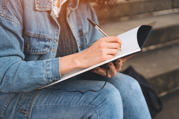 Person Sitting on Steps Writing in Notebook With Pen in Hand During Daylight Hours