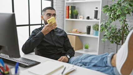 A young bearded man using a smartphone in a modern office setting, conveying a professional and connected atmosphere.