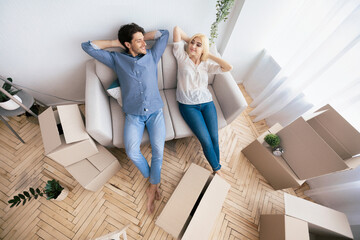 A young couple rests on a sofa in their new home, surrounded by moving boxes.