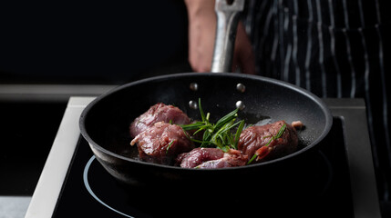 Professional chef cooking beef steak in frying pan on stove in restaurant kitchen