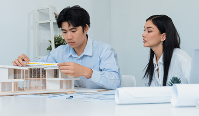Portrait of cooperative engineer team working together to measure house model by using ruler and...