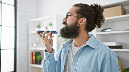 Hispanic man with beard using smartphone in modern office, showing technology and communication in...
