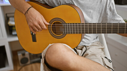 Obraz premium A man playing an acoustic guitar indoors, focused on his hands strumming strings, creating a musical atmosphere