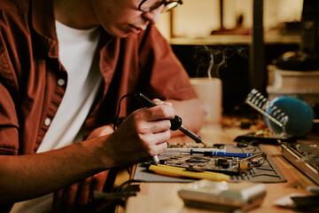 Medium close up of male hand holding small soldering iron to give new life to old laptop