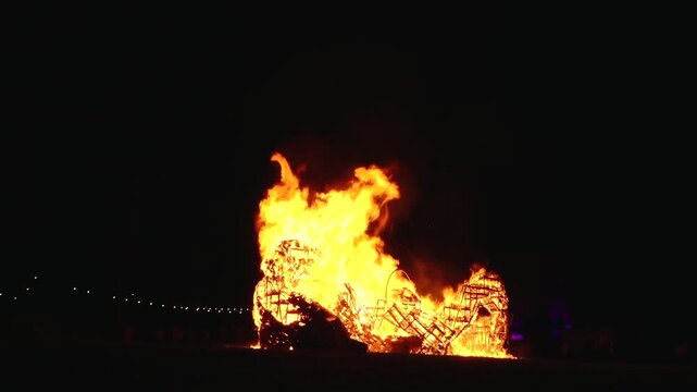 A dramatic image of a fierce fire burning intensely against the dark night sky. The bright orange and yellow flames highlight the raw energy and destructive power of the blaze.