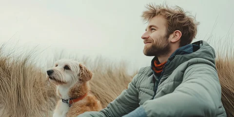 Mann sitzt mit seinem Hund in Dünenlandschaft und lächelt zufrieden © stockmotion