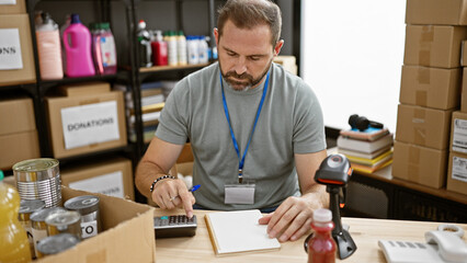 Mature man calculates donations in a warehouse interior.
