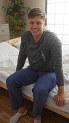 Handsome young man sitting in casual clothes on bed over white wall background