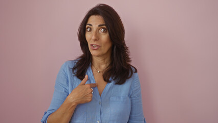 Woman pointing to herself with a surprised expression against an isolated pink background, displaying a middle-aged, hispanic, mature appearance
