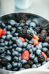 Freshly washed blueberries and blackberries with sliced strawberries in a metal bowl