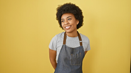 Smiling african american woman with curly hair wearing a denim apron against a yellow background