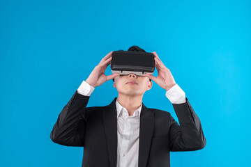 Smiling Asian businessman looking thorough VR connecting to business world report in futuristic metaverse, analyzing innovation technology ads in virtual reality isolated blue copyspace. Contrivance.