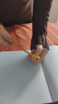 Primer plano de unas manos de mujer con un sacapuntas y un l&aacute;piz encima de unas hojas de papel con cuadros de un cuaderno escolar. Video vertical.