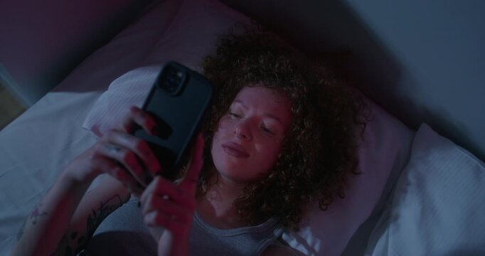 A man uses a mobile phone lying on the bed. Dark room, home interior