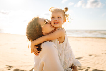 Mommy walks with her daughter on beach during holiday vacation at sunset. Travel, tourism, weekend...