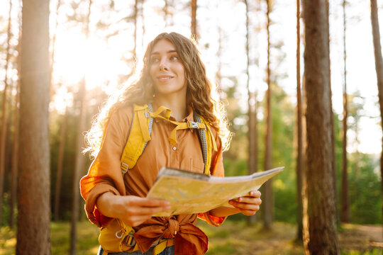 Young woman holding map in forest. Relaxed woman hiker looking navigation searching route. Hiking concept.