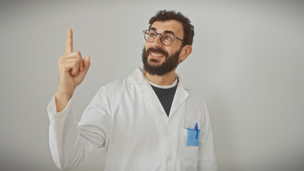 Naklejka premium A cheerful bearded man in a lab coat pointing up isolated against a white background.