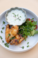 Delicious fried chicken wings with yogurt sauce and greens