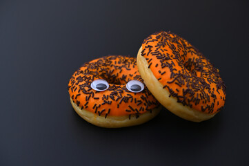 two orange donuts with eyes on a black background close-up