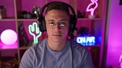 A handsome hispanic man with glasses and headphones in a vibrant gaming room at night.