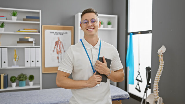 Smiling young hispanic man with glasses, standing confidently in a medical clinic.