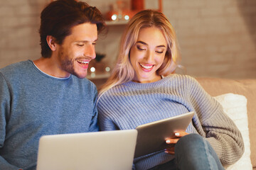 Modern Relationship. Relaxed Couple Using Tablet And Laptop Computers Sitting On Couch Indoor. Selective Focus
