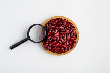 Red beans in a wooden bowl and a magnifying glass on a light background. Raw beans, vegetarian foods. Product quality control.