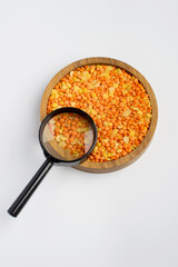 Mix red and orange lentils in a wooden bowl and magnifying glass on a light background. Raw beans, vegetarian foods. Product quality control.