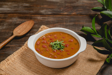 bowl of traditional colombian frijoles bean soup on yute and rustic wooden background
