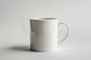 Fototapeta premium A simple white ceramic mug with a rounded handle, photographed against a clean white background, highlighting its minimalist and modern design.