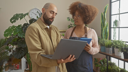 A man and woman discussing business on a laptop in a flower shop surrounded by various plants