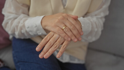 Obraz premium Middle-aged woman with ring sits calmly indoors, hands clasped in a modern room conveying serenity and simplicity.