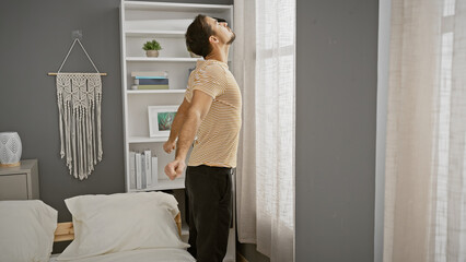 Handsome young hispanic man stretching in a modern bedroom interior with neutral tones.