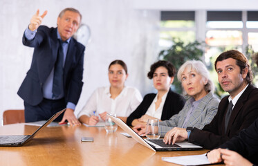 Focused businessman sitting at table in office, listening attentively to presentation of partners during meeting