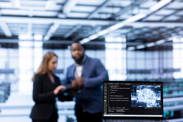 Focus on laptop in data center used by team of specialists in blurry background updating AI...