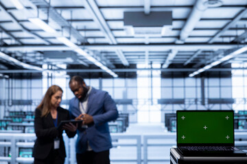 Software developers using green screen laptop in data center, making sure rigs are functioning optimally. Experts in server room using chroma key laptop to monitor energy consumption