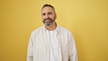 A handsome senior hispanic man with a beard and grey hair posing against an isolated yellow background