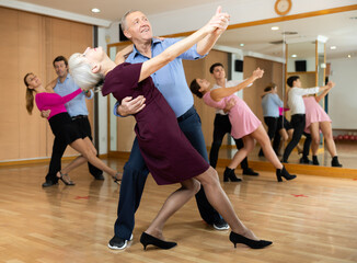 Dynamic aged pair engaging in ballroom dance in dance studio. Pairs training ballroom dance in hall