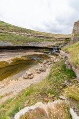 Picturesque waterfall flowing over layered rock formations with lush green moss in Cantabria, Spain. Ideal for nature, travel, and landscape themes.