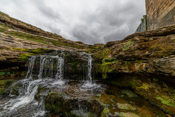 Picturesque waterfall flowing over layered rock formations with lush green moss in Cantabria, Spain. Ideal for nature, travel, and landscape themes.