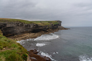 Majestic coastal cliffs with layered rock formations and lush greenery overlooking the sea in Cantabria, Spain. Perfect for landscape, travel, and nature themes.