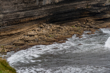 Majestic coastal cliffs with layered rock formations and lush greenery overlooking the sea in Cantabria, Spain. Perfect for landscape, travel, and nature themes.