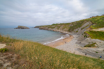 Beautiful sunset over Playa de la Arn&iacute;a, featuring dramatic skies, rocky shoreline, and coastal homes in Cantabria, Spain. Perfect for seascape, travel, and nature themes.