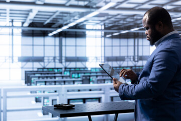 Engineer in data center using tablet to identify and solve technical issues related to data center infrastructure. IT professional managing, maintaining and securing server room environment