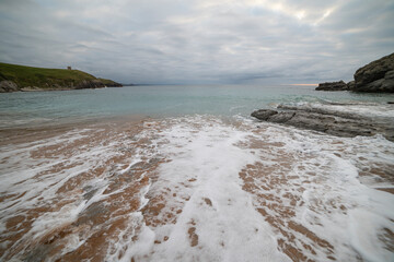 Tranquil scene of Tagle Beach in Cantabria, Spain, showcasing rugged rocks, gentle waves, and an expansive horizon. Perfect for travel, nature, and coastal themes.