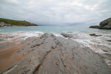 Tranquil scene of Tagle Beach in Cantabria, Spain, showcasing rugged rocks, gentle waves, and an expansive horizon. Perfect for travel, nature, and coastal themes.