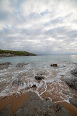 Tranquil scene of Tagle Beach in Cantabria, Spain, showcasing rugged rocks, gentle waves, and an expansive horizon. Perfect for travel, nature, and coastal themes.