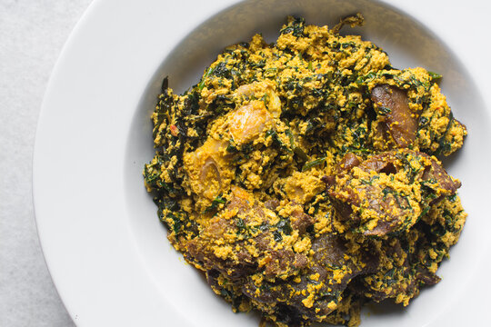 overhead view of Nigerian egusi soup with fish and beef in a white plate, egusi vegetable soup in a large dinner plate, traditional egusi soup in a white dish