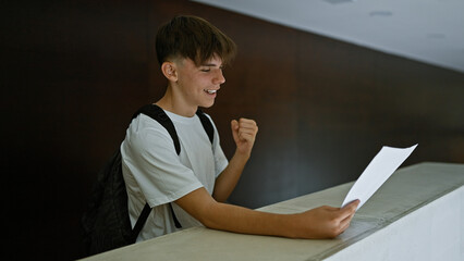 A joyful teenage boy with a backpack celebrates good news reading a paper at school
